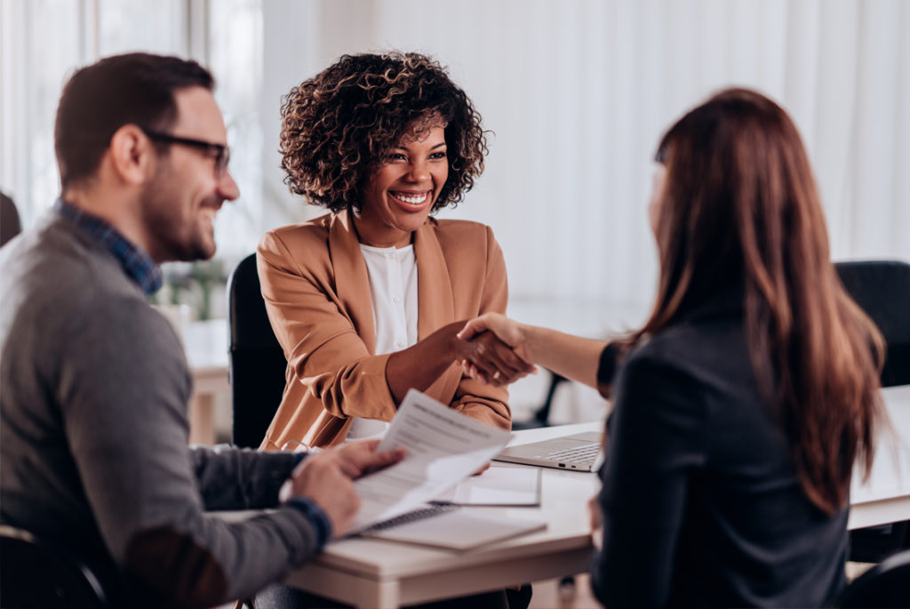 Three business professionals at a meeting, two women shaking hands